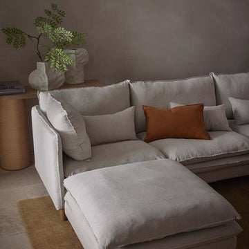 Aura upholstered ottoman in natural Belgian linen with plush feather cushion and solid oak legs for luxury living room seating